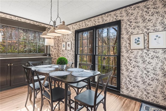 dining area featuring wallpapered walls, ornamental molding, baseboards, and light wood finished floors