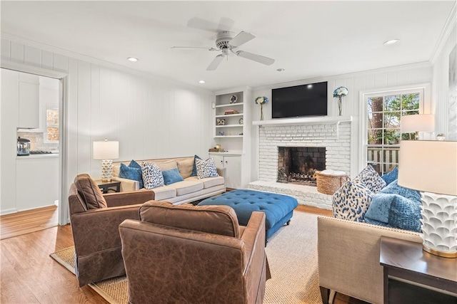 living area with crown molding, a fireplace, wood finished floors, a ceiling fan, and built in features