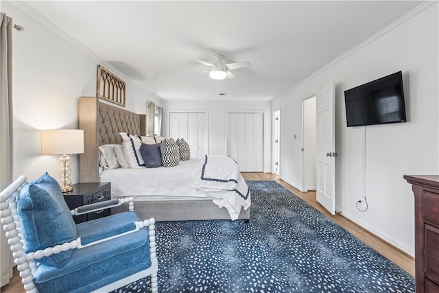 bedroom featuring a ceiling fan, wood finished floors, multiple closets, baseboards, and ornamental molding