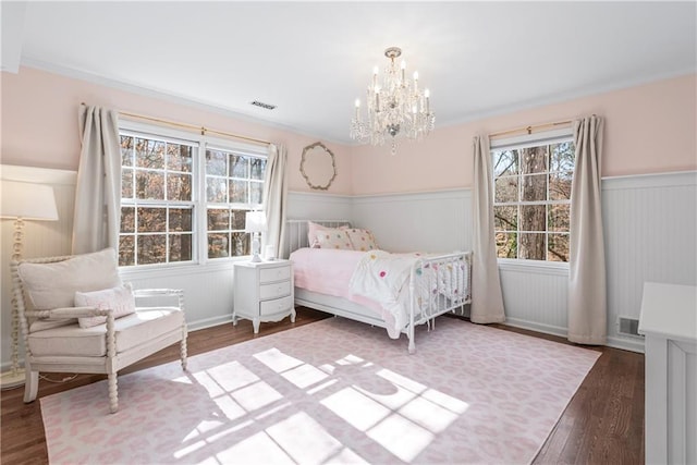 unfurnished bedroom featuring wood finished floors, visible vents, a chandelier, and wainscoting