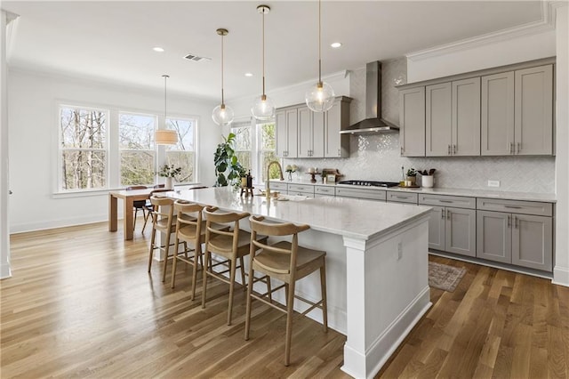 kitchen featuring gray cabinetry, a breakfast bar, wall chimney exhaust hood, wood finished floors, and tasteful backsplash