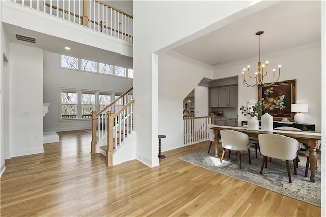dining room with stairway, a chandelier, light wood finished floors, a high ceiling, and baseboards