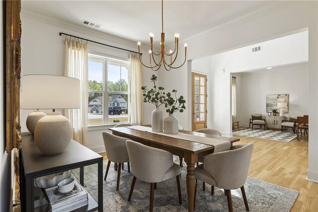 dining area featuring an inviting chandelier, light wood-style floors, visible vents, and crown molding