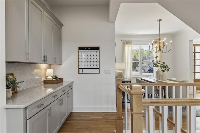 interior space with wood finished floors, a notable chandelier, baseboards, backsplash, and gray cabinetry