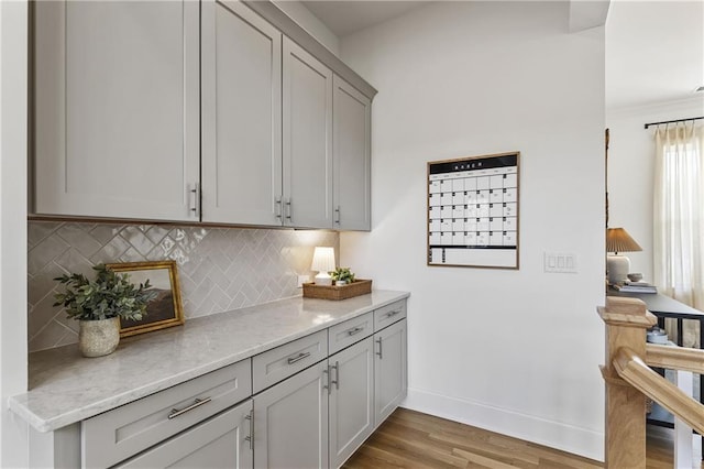 bar with light wood-type flooring, tasteful backsplash, and baseboards