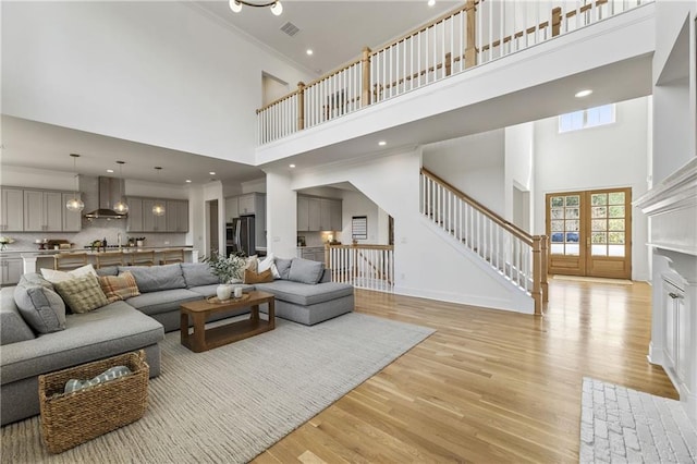 living area with crown molding, light wood-type flooring, visible vents, stairway, and a towering ceiling