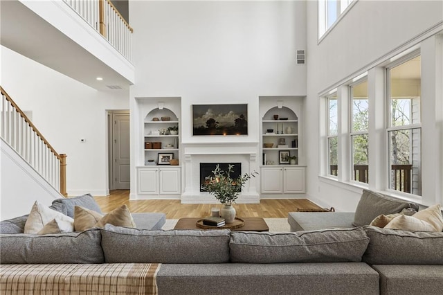 living room featuring stairs, visible vents, light wood-type flooring, and a high ceiling