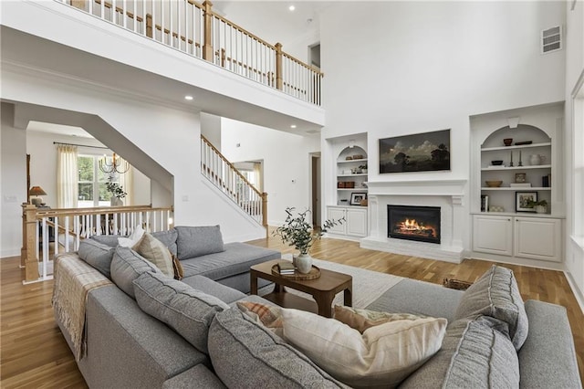 living area with wood finished floors, visible vents, built in features, a high ceiling, and baseboards