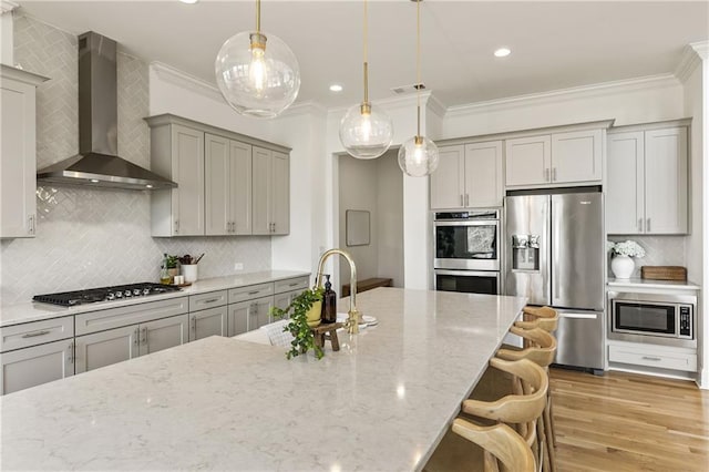 kitchen with ornamental molding, stainless steel appliances, wall chimney range hood, and gray cabinets
