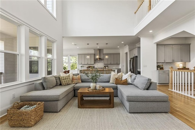 living room featuring light wood finished floors, ornamental molding, a high ceiling, and recessed lighting