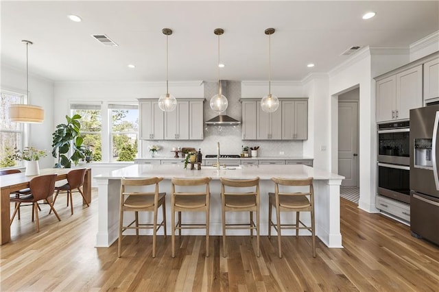 kitchen with light countertops, wall chimney exhaust hood, visible vents, gray cabinetry, and appliances with stainless steel finishes