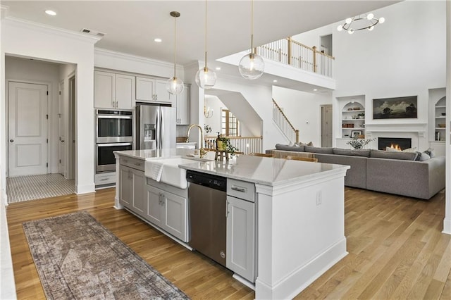 kitchen with a sink, built in features, an island with sink, crown molding, and appliances with stainless steel finishes