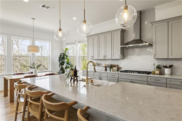 kitchen with gas cooktop, wall chimney exhaust hood, crown molding, decorative backsplash, and gray cabinetry
