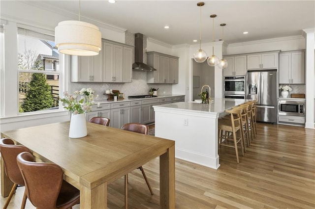 kitchen with gray cabinetry, a healthy amount of sunlight, appliances with stainless steel finishes, and wall chimney exhaust hood