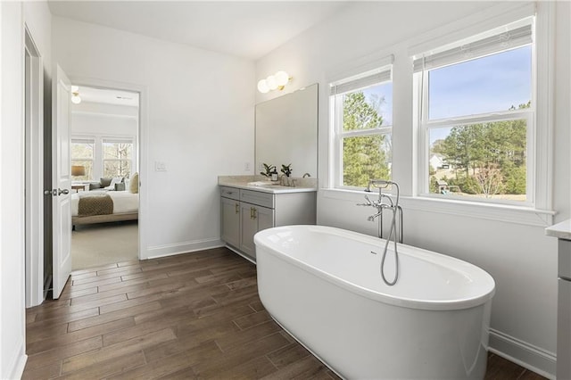 ensuite bathroom featuring baseboards, ensuite bathroom, vanity, a freestanding bath, and wood finished floors