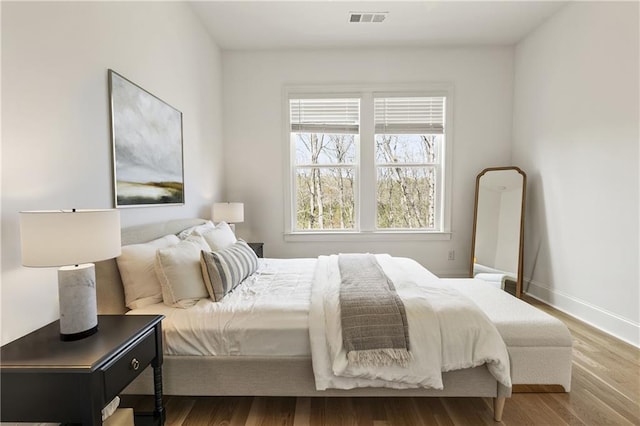 bedroom with baseboards, visible vents, and wood finished floors