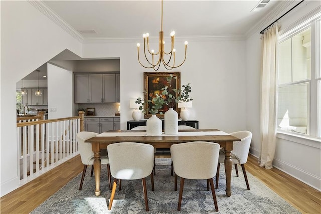 dining room with light wood finished floors, a chandelier, baseboards, and ornamental molding