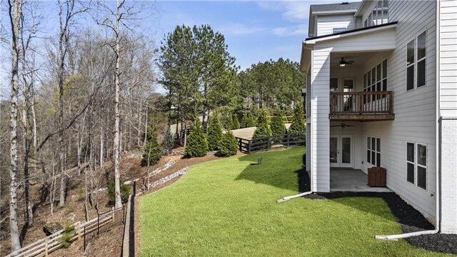 view of yard featuring fence, french doors, a balcony, a patio, and a ceiling fan