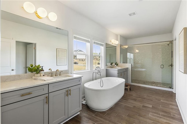 bathroom featuring wood finished floors, vanity, visible vents, a stall shower, and a soaking tub