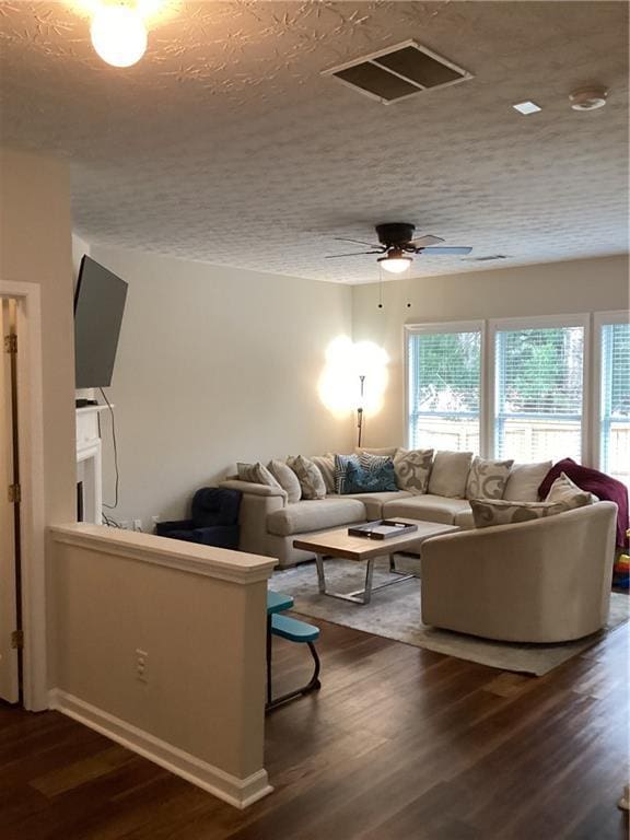 living room with a textured ceiling, dark wood-type flooring, visible vents, and ceiling fan