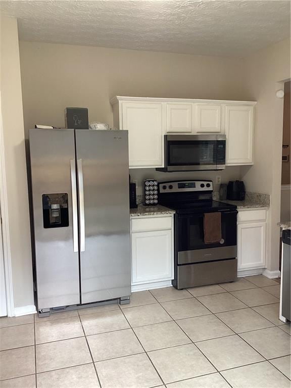 kitchen featuring light tile patterned floors, white cabinets, appliances with stainless steel finishes, and light stone countertops