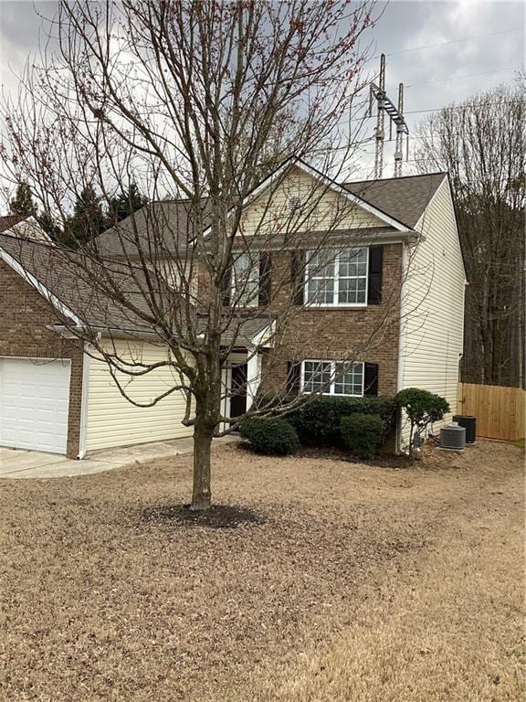 colonial home featuring central AC unit, fence, an attached garage, concrete driveway, and brick siding