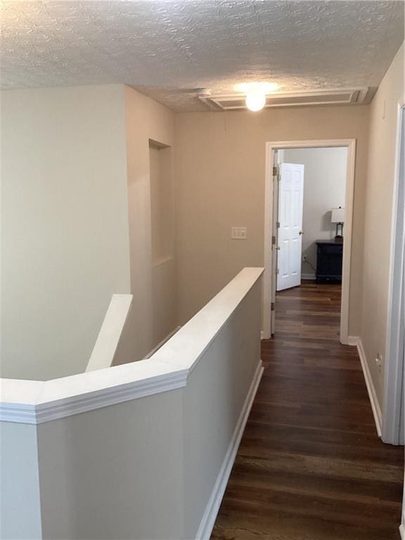 hallway featuring baseboards, an upstairs landing, a textured ceiling, and dark wood-style floors