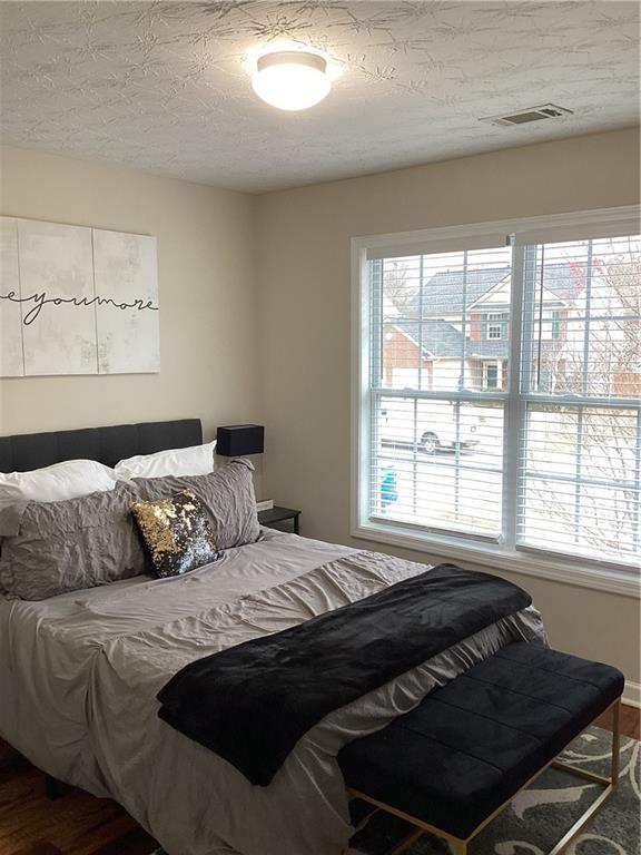 bedroom with visible vents, multiple windows, a textured ceiling, and wood finished floors