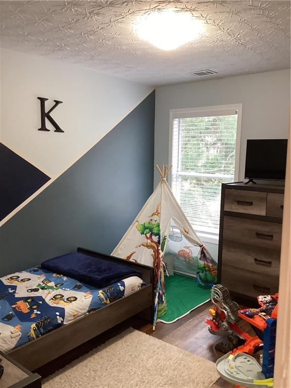 bedroom with wood finished floors, visible vents, and a textured ceiling