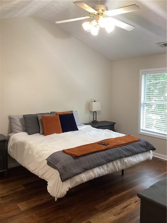 bedroom featuring lofted ceiling, a ceiling fan, visible vents, and dark wood-style flooring