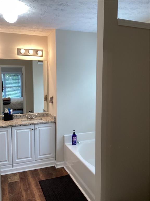 ensuite bathroom with ensuite bathroom, a textured ceiling, wood finished floors, a bath, and vanity