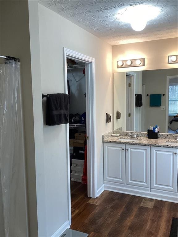 full bathroom featuring a sink, a textured ceiling, wood finished floors, and a spacious closet