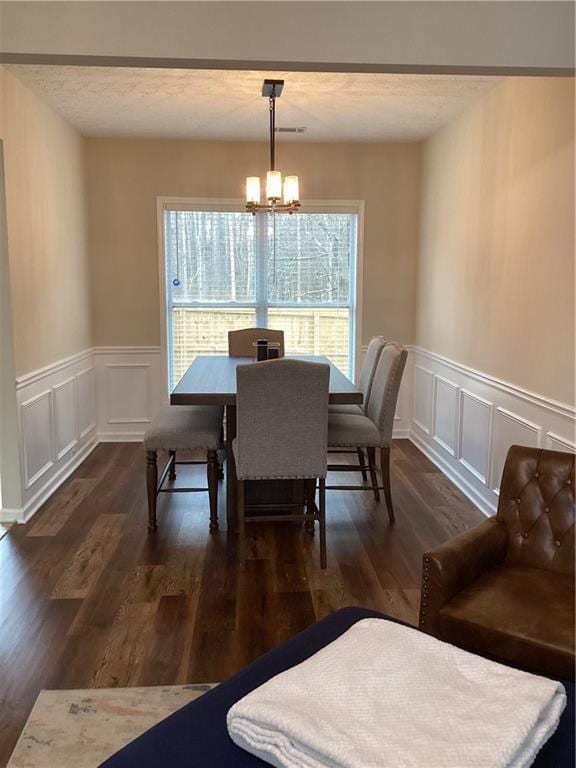 dining space featuring a decorative wall, dark wood-type flooring, an inviting chandelier, and a textured ceiling