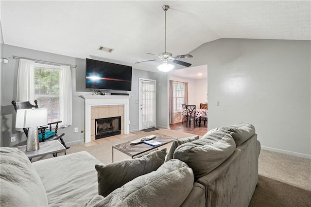 carpeted living room with ceiling fan, lofted ceiling, and a tiled fireplace