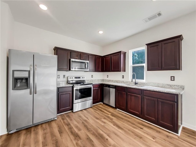 kitchen with light stone counters, light hardwood / wood-style flooring, stainless steel appliances, and sink