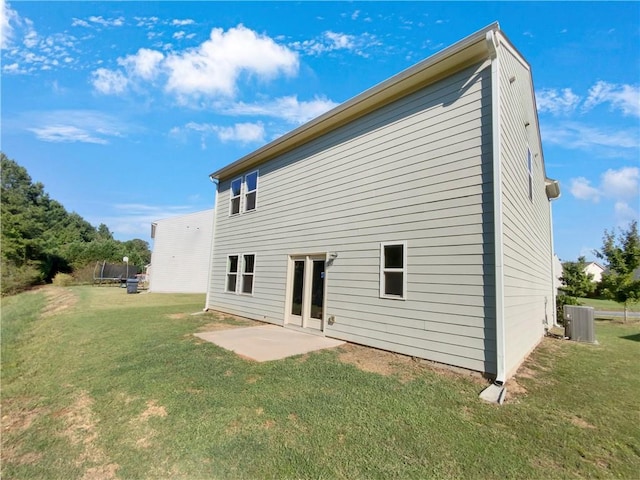 rear view of property with a trampoline, a lawn, a patio area, and central AC unit