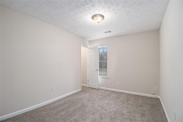 carpeted spare room with visible vents, baseboards, and a textured ceiling