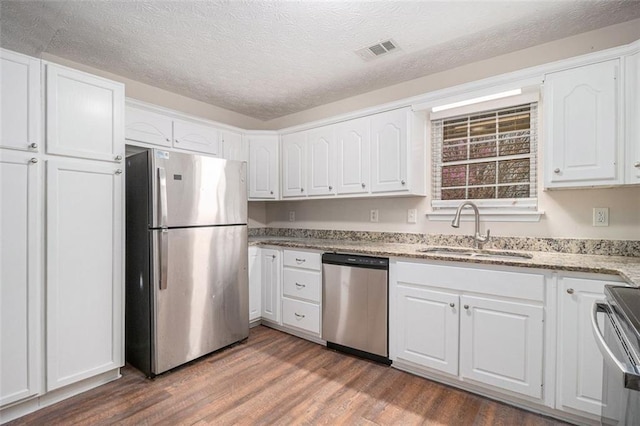 kitchen with visible vents, white cabinets, wood finished floors, stainless steel appliances, and a sink