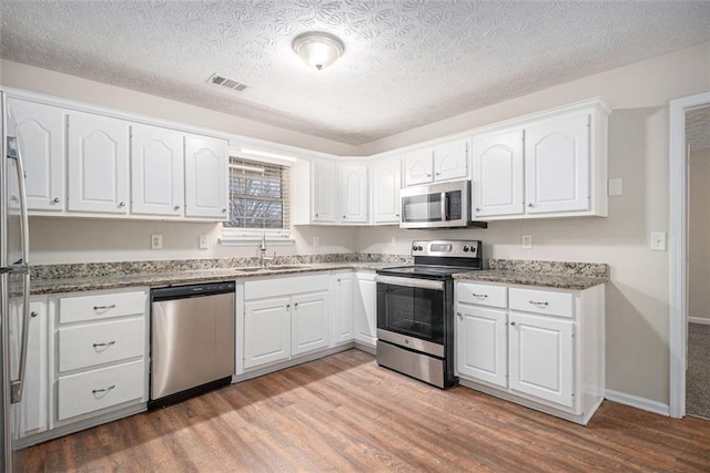 kitchen with visible vents, appliances with stainless steel finishes, white cabinets, a sink, and light wood-type flooring