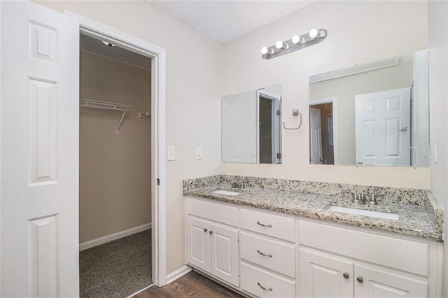 full bath with double vanity, a spacious closet, baseboards, and a sink