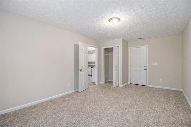 unfurnished bedroom featuring a closet, visible vents, light carpet, a textured ceiling, and baseboards