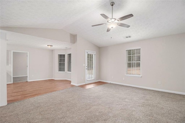 carpeted empty room featuring visible vents, vaulted ceiling, a textured ceiling, ceiling fan, and baseboards