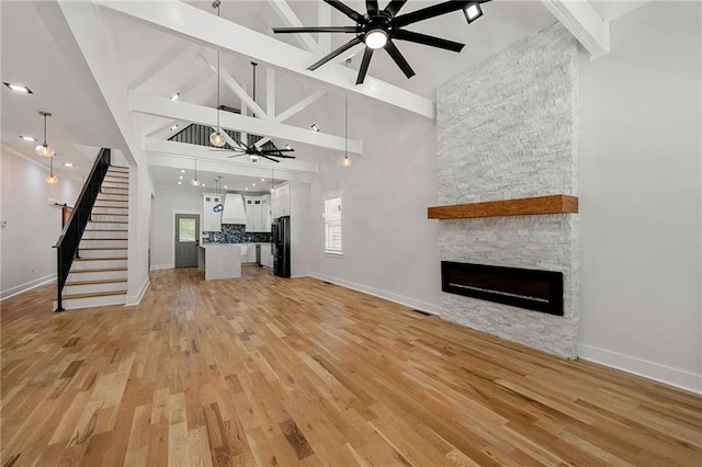 unfurnished living room with high vaulted ceiling, a fireplace, light hardwood / wood-style floors, and ceiling fan