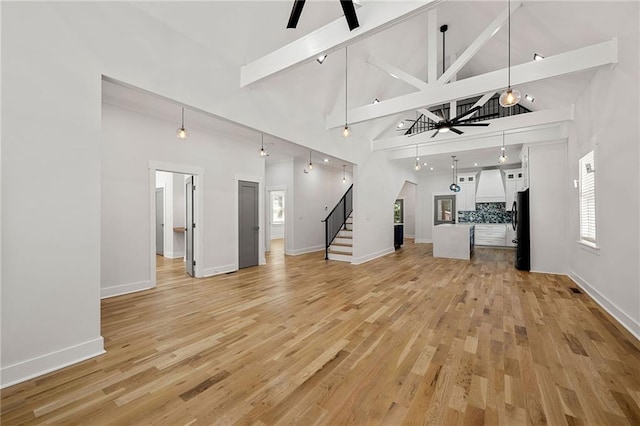 unfurnished living room featuring beam ceiling, high vaulted ceiling, light wood-type flooring, and ceiling fan