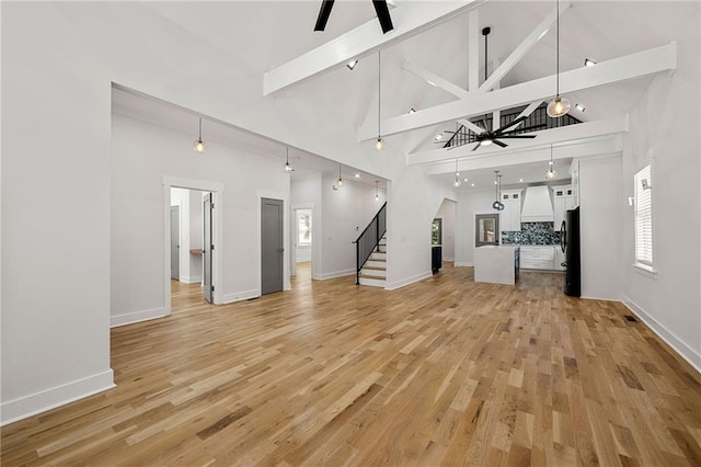 unfurnished living room featuring light wood-style floors, ceiling fan, high vaulted ceiling, and stairway