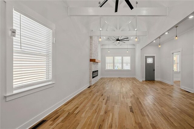 unfurnished living room featuring ceiling fan, a healthy amount of sunlight, beam ceiling, and hardwood / wood-style floors