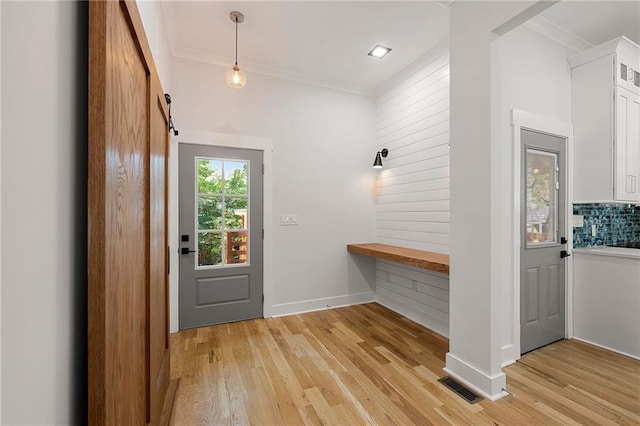 doorway to outside with light hardwood / wood-style floors, ornamental molding, and a barn door