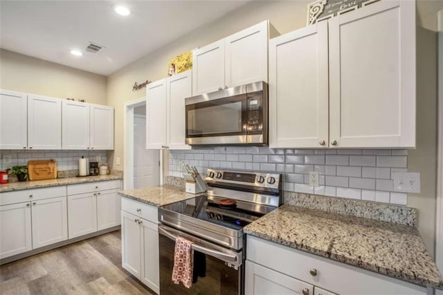 kitchen featuring light wood finished floors, white cabinets, stainless steel appliances, backsplash, and recessed lighting