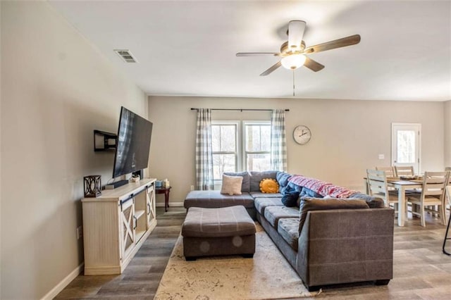 living room with dark wood-style floors, baseboards, visible vents, and ceiling fan