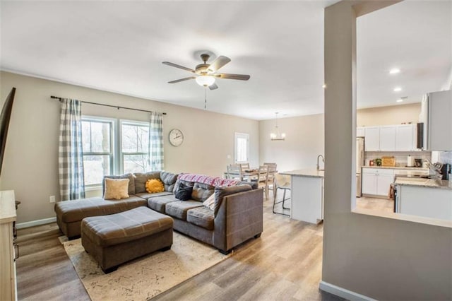 living area featuring ceiling fan with notable chandelier, recessed lighting, baseboards, and light wood-style floors